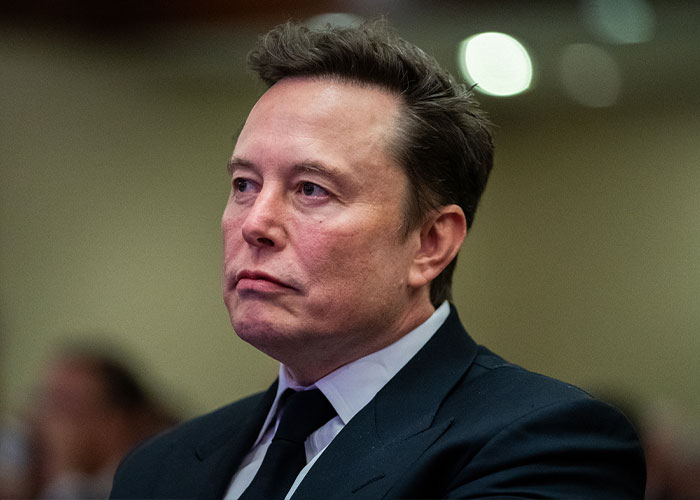 Close-up of Elon Musk in a suit, often discussed during his recent Spaceport visit regarding scoliosis.