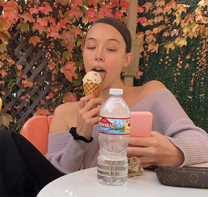 A young woman eating an ice cream cone, under autumn leaves.