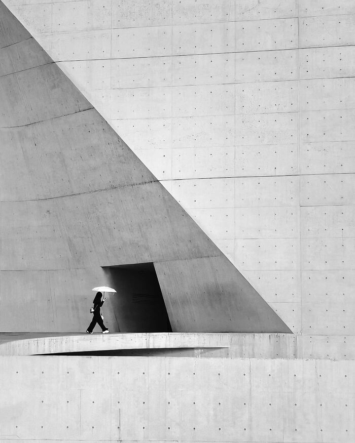 A photographer captures everyday architecture into a bold minimalist scene of a person with an umbrella walking past a concrete wall with a triangular shadow.