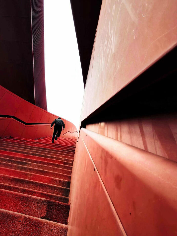 A photographer captures minimalist architecture with a person running up vibrant red stairs, creating bold scenes.