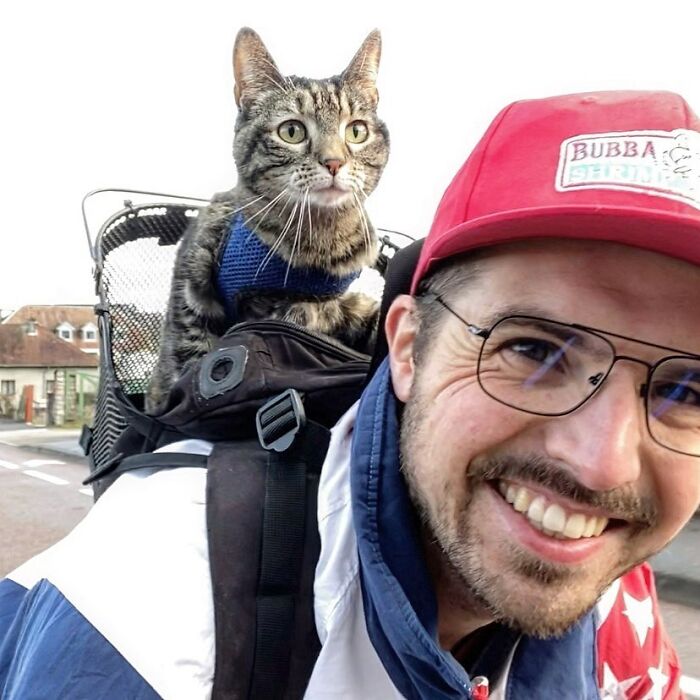A happy owner and his cat going on adventures, the cat riding in a backpack on the owner's back.