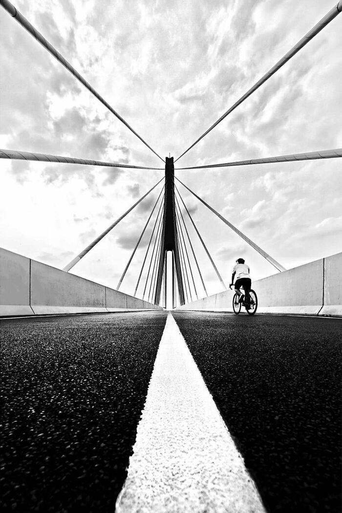 A minimalist black and white scene of a person cycling on a bridge, showcasing bold architecture and leading lines.