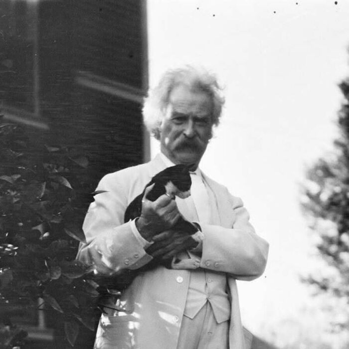Vintage cat photo of Mark Twain holding a small black and white kitten outdoors