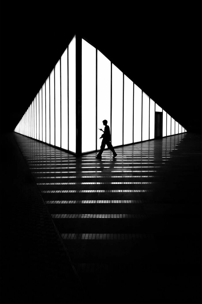 A photographer captures everyday architecture into a bold minimalist scene of a silhouetted person walking down a hallway with bright vertical lights.