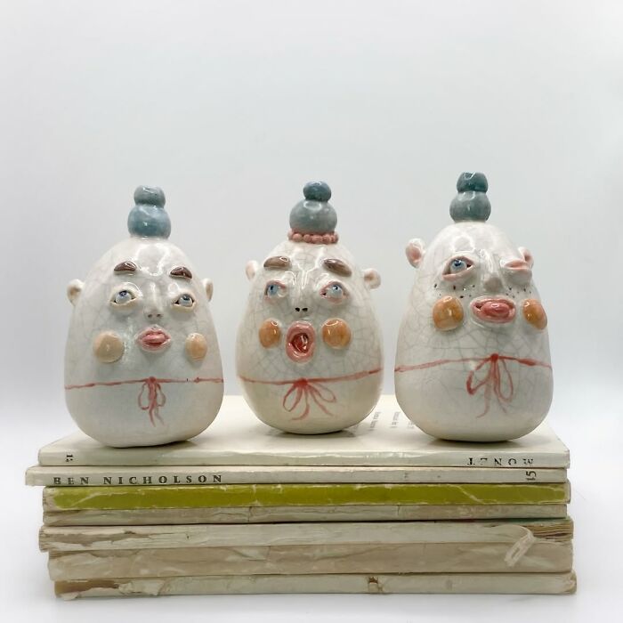 Three small weird ceramic sculptures resembling funny egg-shaped characters on top of vintage books.