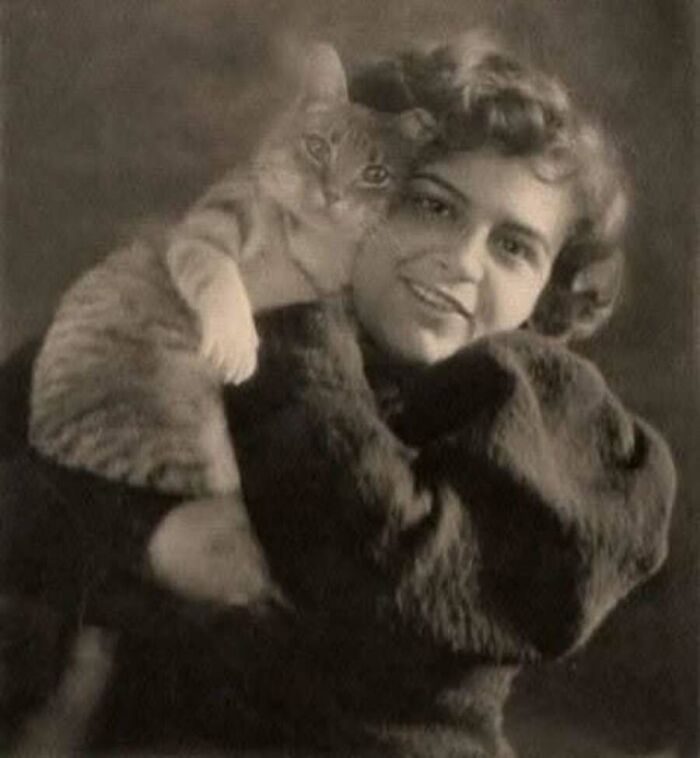 Vintage cat photo of a smiling woman with styled hair holding her tabby cat close to her shoulder