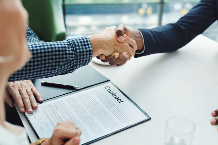 Two professionals shaking hands over a business contract at a table