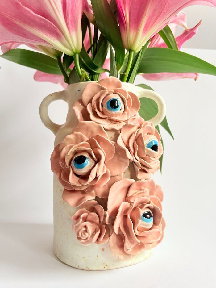Creative ceramic flower vase decorated with pink sculpted roses that have realistic blue eyeballs inside.