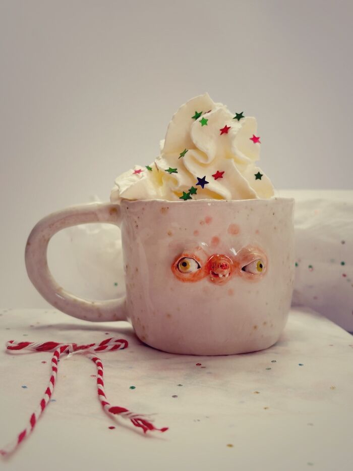 Weird ceramic sculptures coffee mug featuring a hand-sculpted face, topped with whipped cream and star sprinkles.