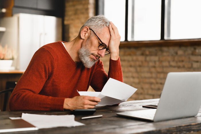 An older man looking stressed at a desk, illustrating dumb ways people ruin their lives.
