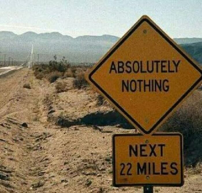 A funny road sign in a desert landscape reads Absolutely Nothing Next 22 Miles, amusing travelers.