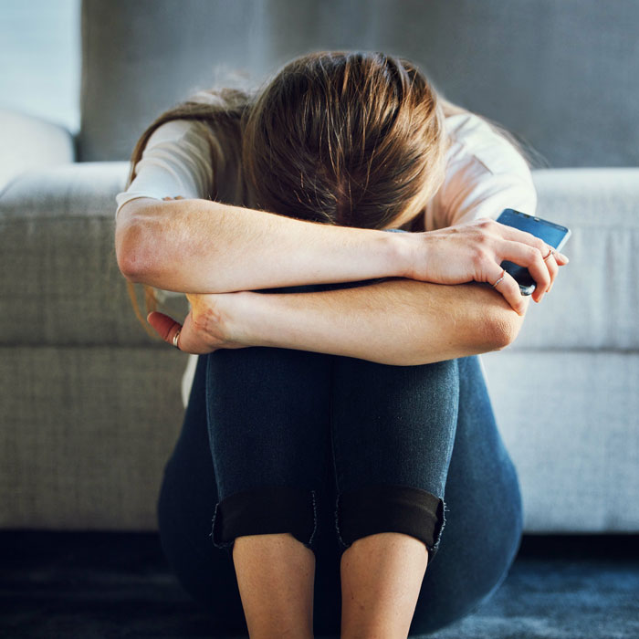 A distressed woman curled up on the floor in severe pain holding her phone