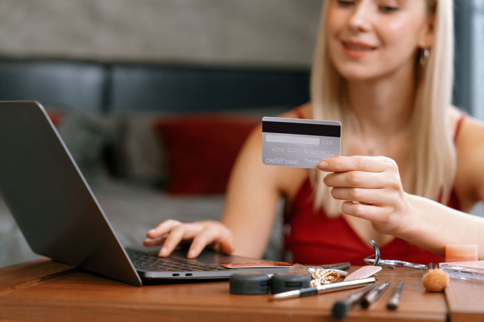 A woman holding a credit card while using her laptop, a scenario common for divorced people