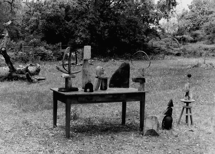 A collection of Heather Chontos creative art sculptures displayed on and around a wooden table outdoors.