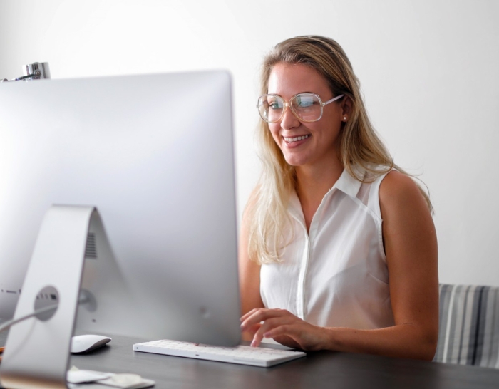 A smiling employee wearing glasses works diligently at a computer, making her supervisors look bad. A smiling employee wearing glasses works diligently at a computer, making her supervisors look bad.