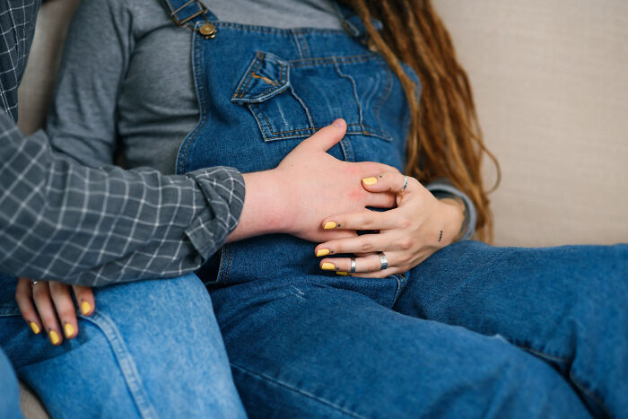 A couple holding hands on a pregnant belly, suggesting dumb ways people ruin their lives.