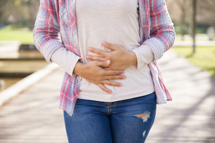 A woman holds her stomach outdoors, symbolizing a sister gives brother part of her liver. A woman holds her stomach outdoors, symbolizing a sister gives brother part of her liver.