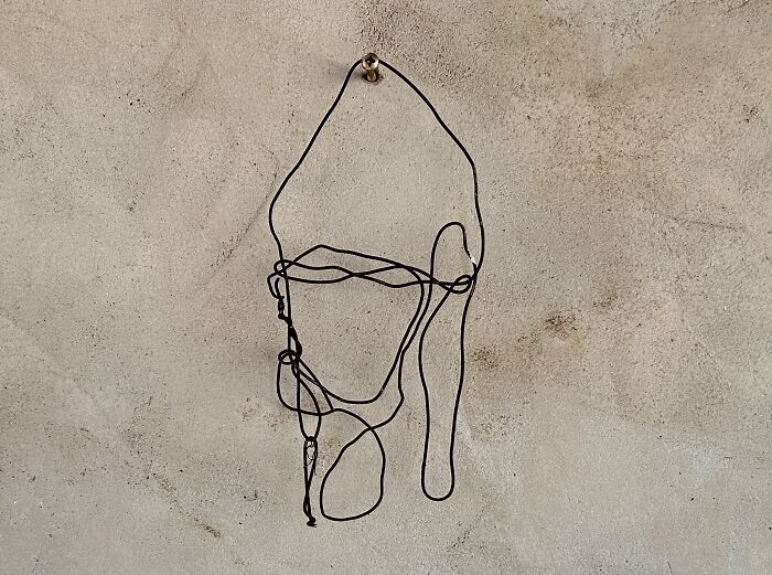 A tangled piece of black wire hanging on a wall, forming an abstract shape in creative art by Heather Chontos.