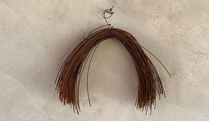 A bundle of rusty wire hanging on a wall, showcasing creative art by Heather Chontos.
