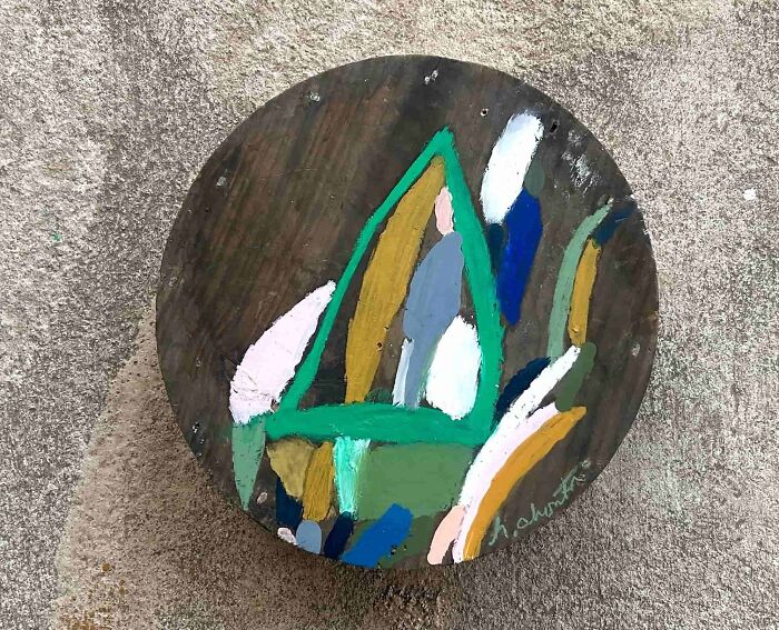 A circular piece of wood with abstract creative art by Heather Chontos in green, yellow, white, and blue.