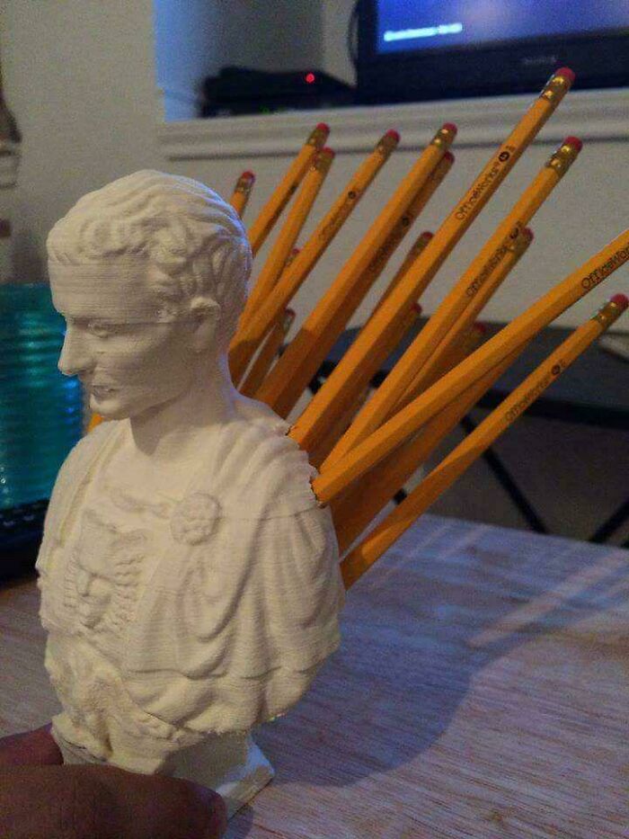A creative 3D printers bust of a classical figure with pencils fanned out like wings from its back.