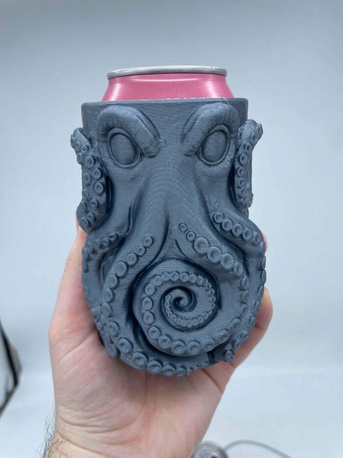 A hand holding a can in an innovative 3D printers octopus-shaped can holder with detailed tentacles.