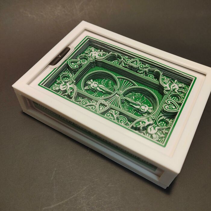 An intricate green and white layered 3D printed art piece, resembling a decorative playing card, sits on a table.