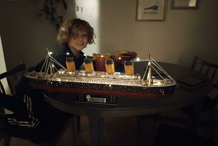A young boy proudly displays a meticulously detailed, lit-up 3D printed Titanic model.