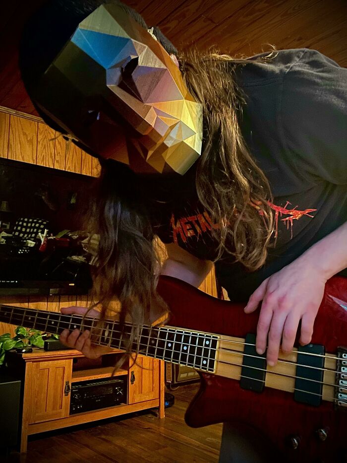 A person wearing a geometric 3D printed mask plays a bass guitar, showcasing brilliant custom creations.