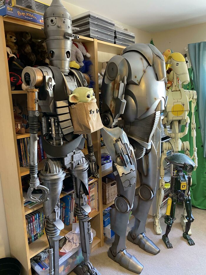 Several life-sized 3D printed robot costumes and models, including Grogu in a pouch, in a room.