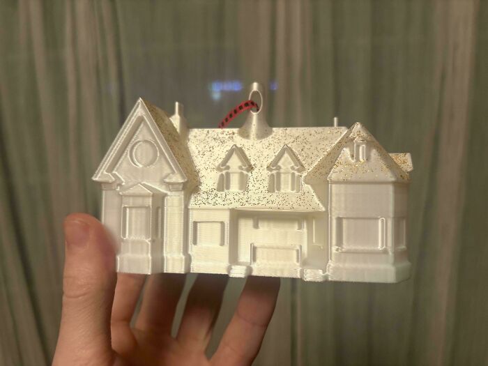 A hand holding a white 3D printed house model with glitter, possibly an ornament.