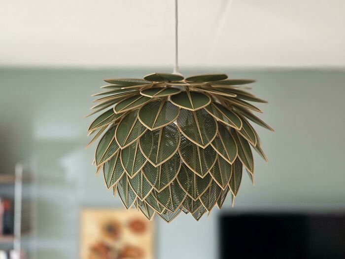A beautiful 3D printed leaf-shaped lampshade in green and gold, hanging in a room.