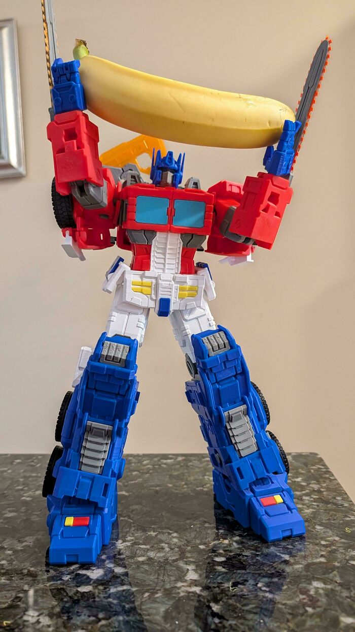 An Optimus Prime action figure holding a banana and a chainsaw, a brilliant and humorous piece made using 3D printers.