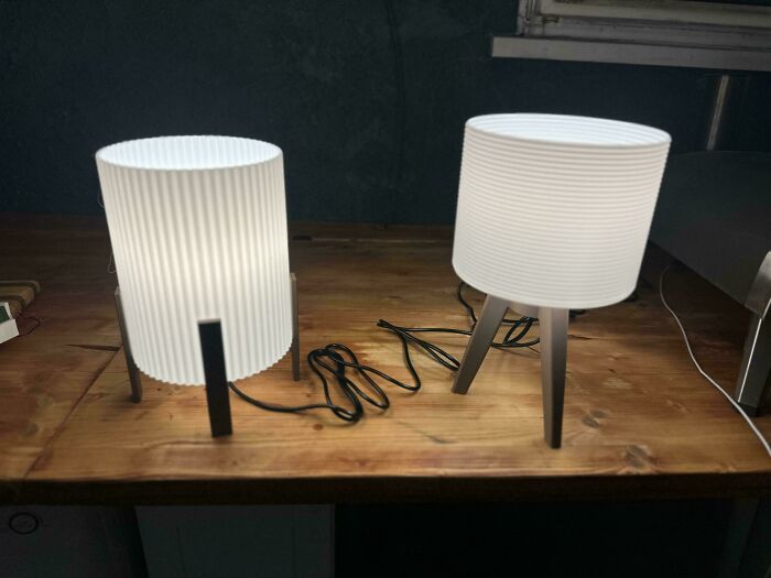 Two minimalist white cylindrical lamps with unique bases, brilliant creations from 3D printers, on a wooden table.