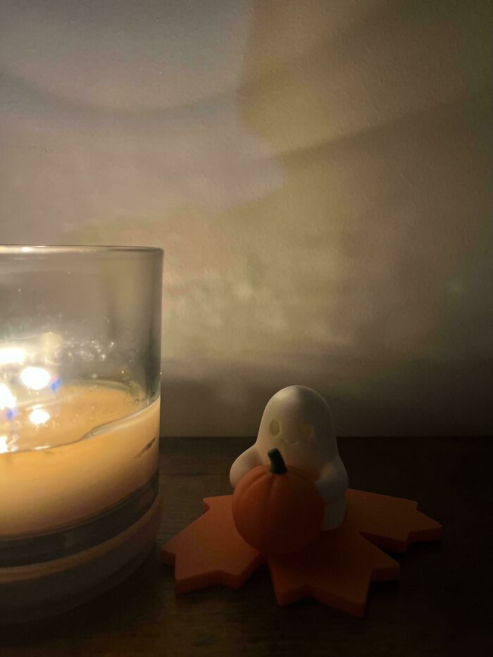 A small ghost figurine holds a pumpkin next to a glowing candle, showcasing brilliant 3D printers creation.