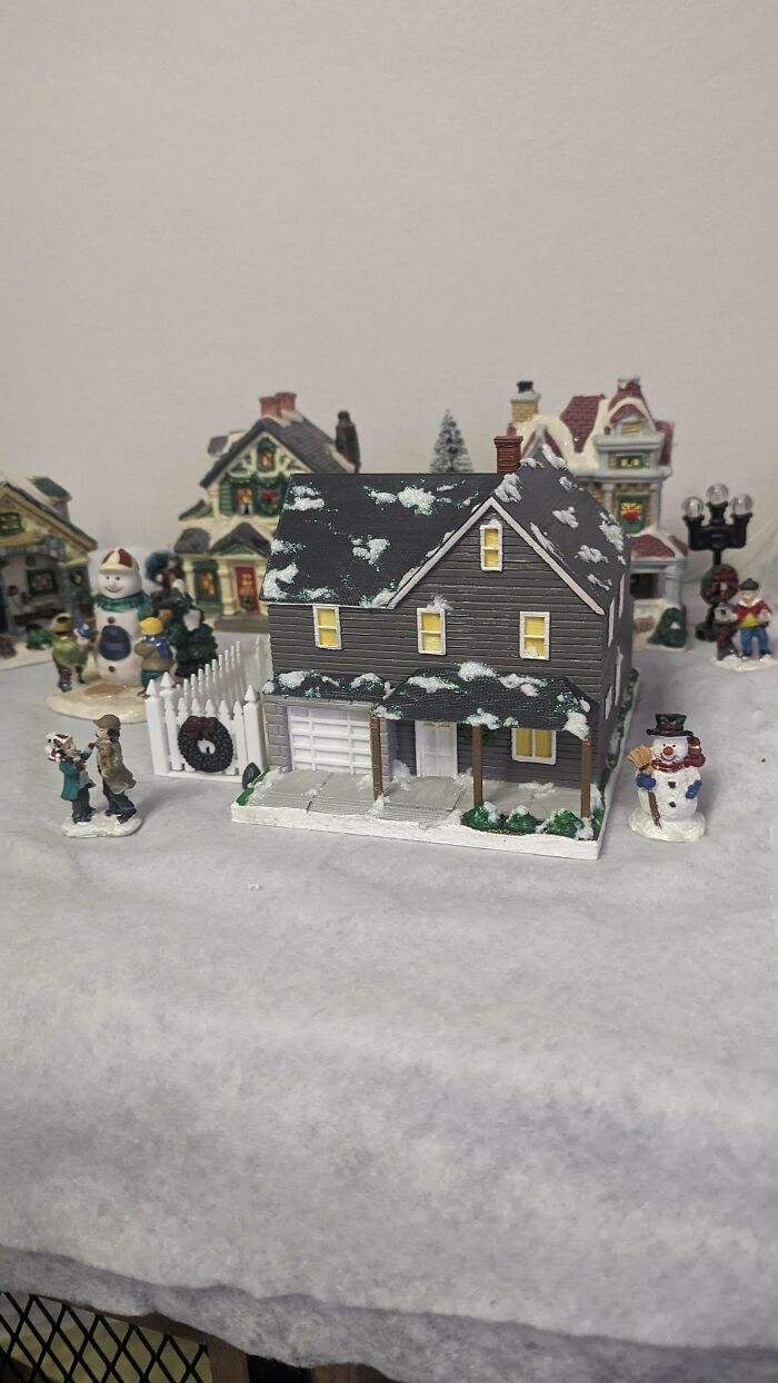 A miniature house with snow-covered roof and tiny figures, brilliant stuff created using 3D printers for a village scene.
