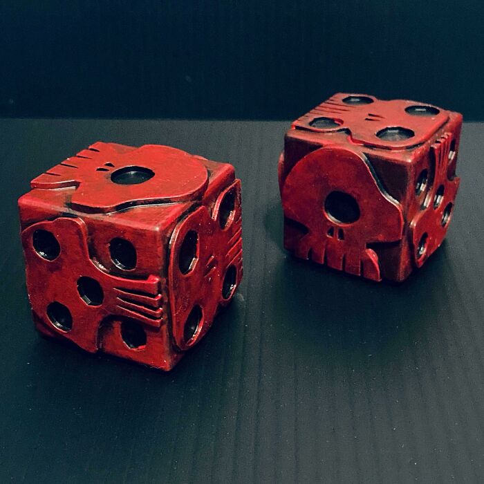 Two red 3D printed dice with skull designs on a dark surface, showcasing brilliant stuff.
