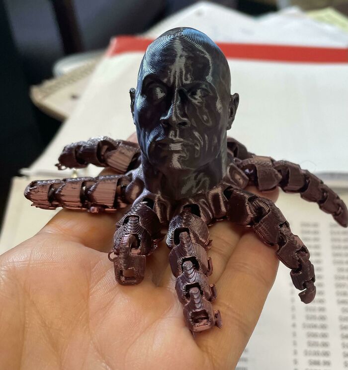 A hand holds a 3D printed figurine of a man's head attached to an octopus body, showing brilliant stuff.