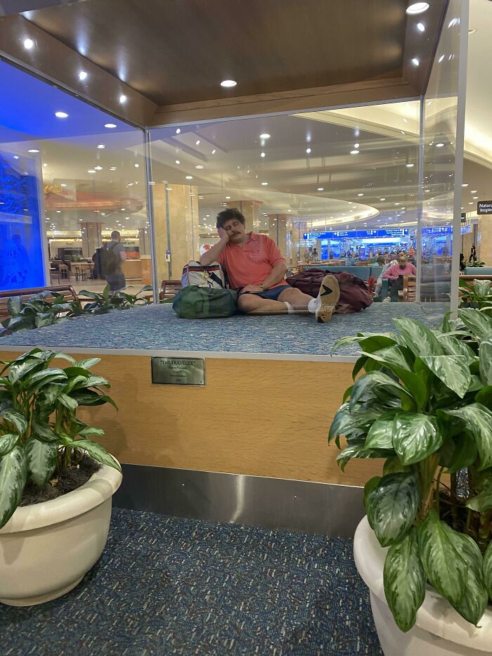 A man sleeping on a raised platform behind glass at the airport, a hilarious and weird thing spotted.