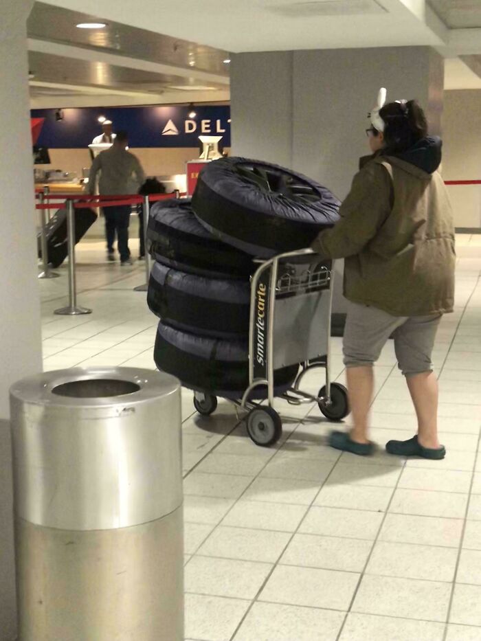 A person with bunny ears pushing a luggage cart stacked with large, round items at the airport, a weird thing spotted.