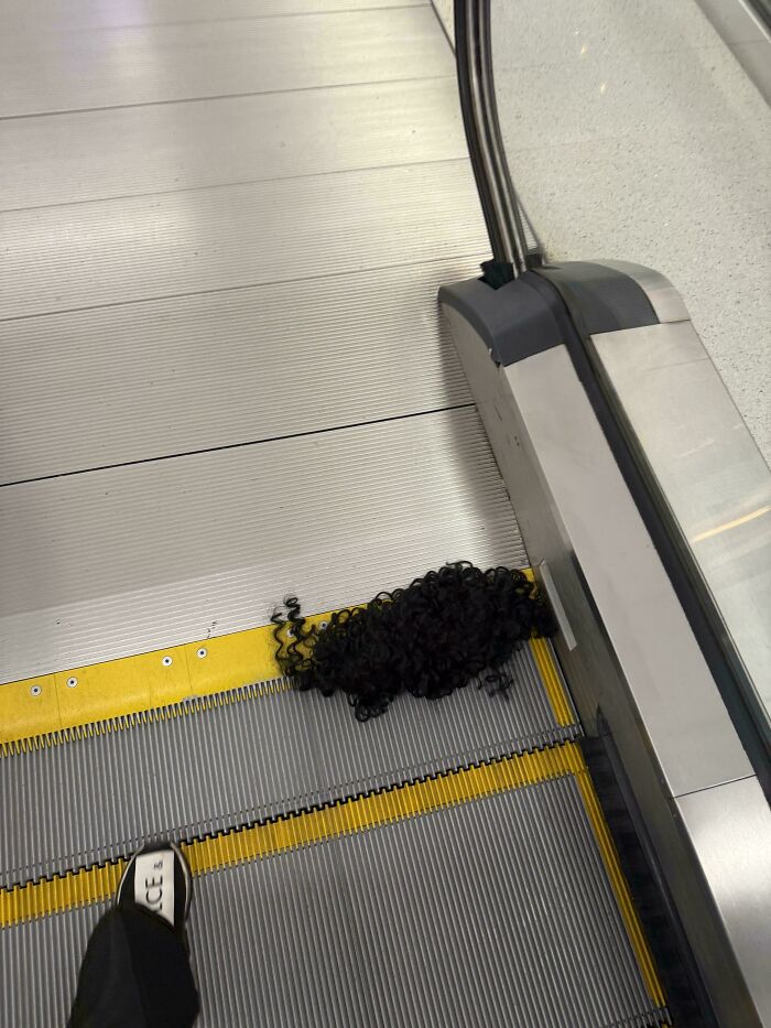 A black curly wig resting on an escalator at the airport, a weird thing spotted.