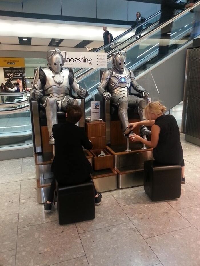 Two robotic figures resembling Cybermen getting their shoes shined at an airport, a weird thing spotted at airports.