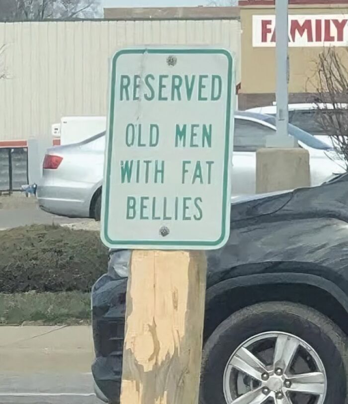 A funny sign that reads RESERVED OLD MEN WITH FAT BELLIES, placed on a wooden post.