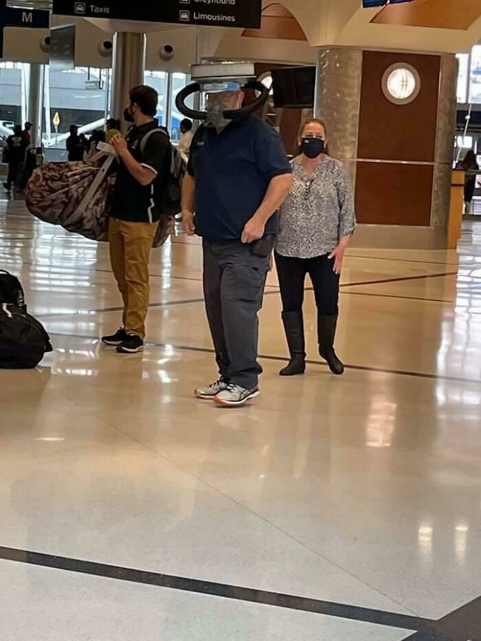 A hilarious thing spotted at airports: a man wearing a large, unusual face shield resembling a bicycle helmet.
