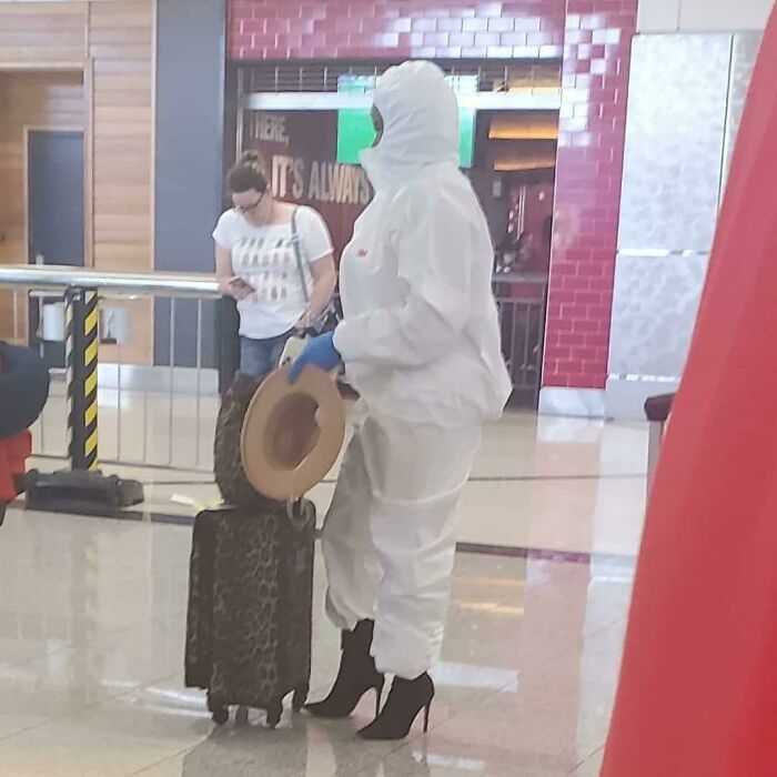 A weird thing spotted at airports: a person in a full white protective suit and high heels, holding a hat.