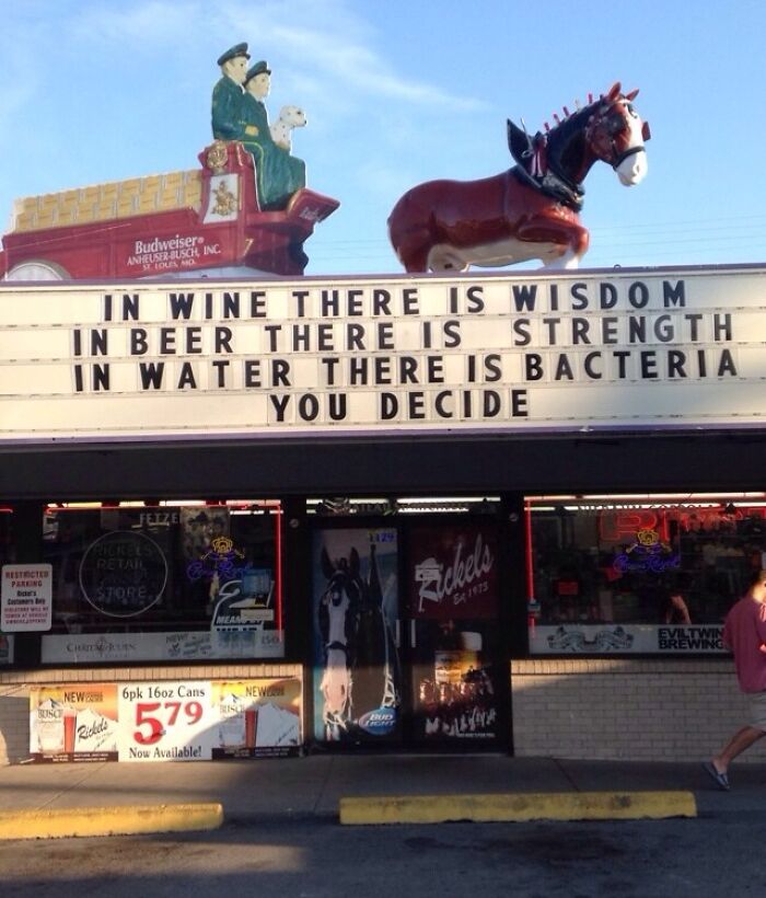 A liquor store sign with funny signs promoting beer for strength and wisdom in wine.