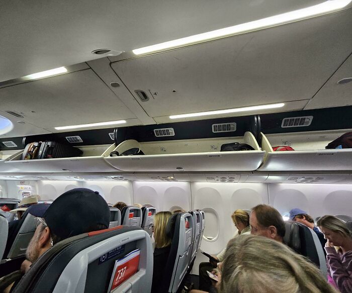 Airplane cabin with passengers and open overhead bins, showing what cabin crew manage.