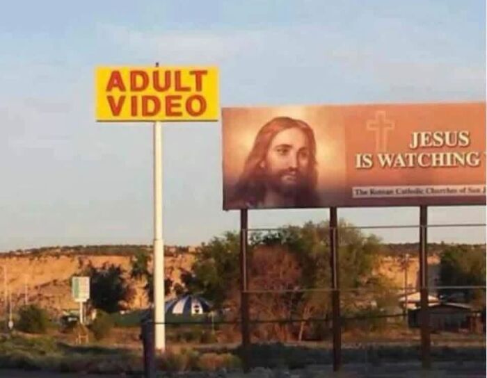 A funny juxtaposition of an Adult Video sign next to a billboard of Jesus is Watching, creating a silly sign.