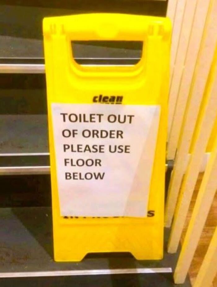 A silly sign on a yellow wet floor cone indicates the toilet is out of order and to use the floor below.