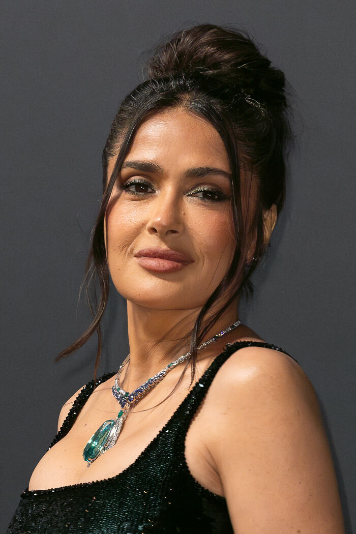 Salma Hayek looking elegant with an updo hairstyle and a dazzling emerald necklace, highlighting her career highlights.